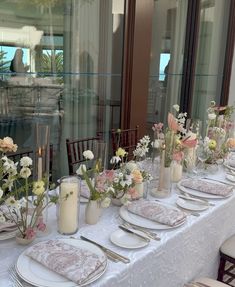 a long table with white and pink flowers in vases, plates and napkins