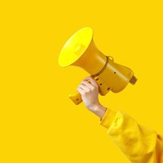 a person holding a yellow megaphone up to their face in front of a yellow background