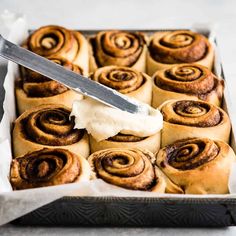 a pan filled with cinnamon rolls covered in icing next to a knife and butter