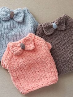 three knitted baby hats with bows on the top and bottom, all in different colors