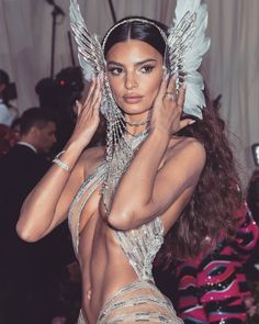 a woman in a silver outfit with wings on her head and hands behind her head