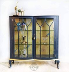 an ornate display cabinet with glass doors and gold trimmings on the top, in front of a white wall