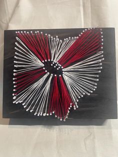 the string art is made with red and white yarn, which are attached to black wood