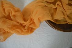 an orange scarf is laying on top of a white sheeted tablecloth with a wooden bowl in the background