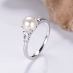 a white pearl and diamond ring sitting on top of a table next to a rock