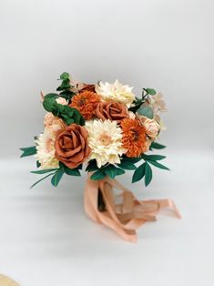 a bridal bouquet with orange and white flowers on a beige ribbon tied around it