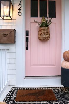 a pink front door with a basket hanging on it's side and two pumpkins