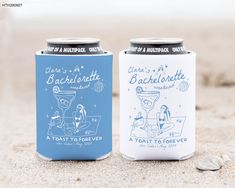 two cans of beer sitting next to each other on top of a sandy beach covered in sand