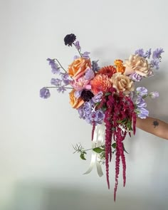 a person holding a bouquet of flowers in their hand with the wall behind them painted white