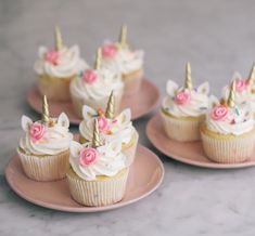 cupcakes with white frosting and pink flowers on them are sitting on plates