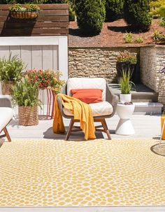 an outdoor area with chairs, potted plants and a yellow rug on the ground