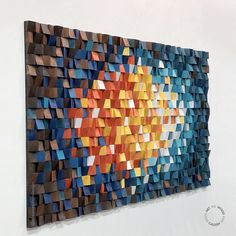 an abstract piece of art made out of wooden blocks and colored paper on the wall