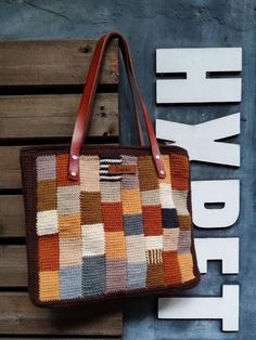 This vintage crochet shoulder bag is hand crocheted with a patchwork design in cotton yarn. It comes in a brown tone with a variety of color shades, including beige, orange, yellow, grey, and cream. The pattern is composed of small individual squares and rectangles. Each is crocheted in a different color, creating a vibrant effect. The crochet bag features dark brown genuine leather straps. It has a cotton lining interior with side pockets and a secure zip closure. The edges of this handmade tot Brown Rectangular Crochet Bag With Leather Handles, Rectangular Brown Crochet Bag With Leather Handles, Brown Crochet Bag With Leather Handles, Brown Crochet Everyday Bag With Leather Handles, Brown Crochet Bag With Leather Handles For Everyday, Brown Hand-knitted Rectangular Bag, Everyday Brown Crochet Bag With Leather Handles, Bohemian Hand-knitted Brown Shoulder Bag, Bohemian Brown Hand-knitted Shoulder Bag