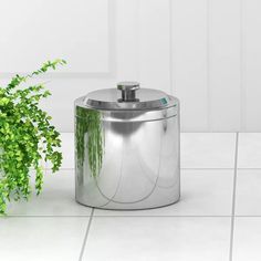 a potted plant sitting on top of a white tile floor next to a stainless steel trash can