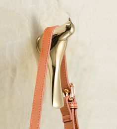 a gold purse hanging on the wall with a pink strap around it's neck