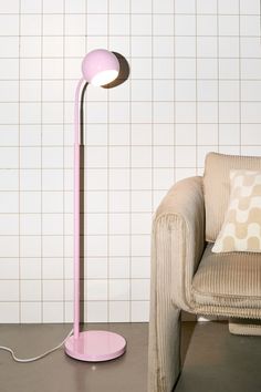 a pink floor lamp sitting next to a couch in a room with white tiles on the walls