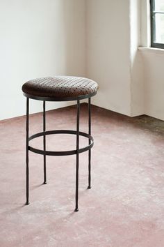 a stool sitting on top of a pink floor in front of a window with an iron frame