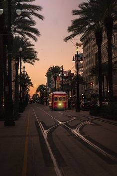 a trolley car traveling down a street next to palm trees and buildings at dusk with lights on