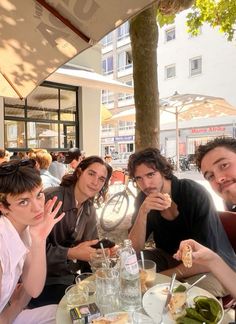 four people sitting at a table with food in front of them and one person holding up her hand