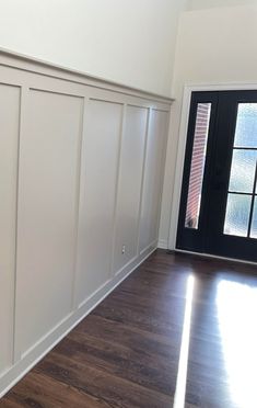 an empty room with wood floors and white walls, black door and window on the far wall