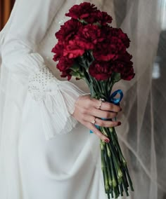 a woman in a white dress holding a bouquet of red carnations on her wedding day