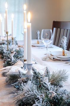 a christmas table setting with white candles and evergreen garland on the dining room table runner