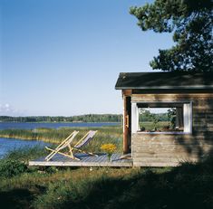 there is a small cabin with a deck on the grass next to it and a lake in the background