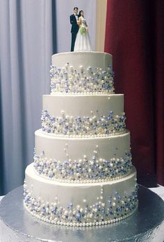 a wedding cake with blue and white decorations on it's tiers, topped with a bride and groom figurine