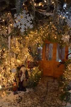 a christmas tree with lights and decorations on it in front of a wooden cabin door