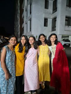 four women standing in front of a building at night with their arms around each other