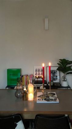 a table with candles and pictures on it in front of a white wall behind two black chairs