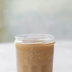 a glass jar filled with brown liquid sitting on top of a white countertop next to a window