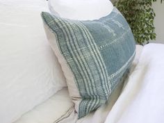 a bed with white sheets and pillows on top of it next to a potted plant