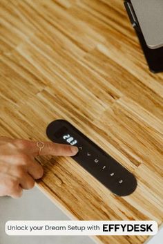 a person pointing at a remote control on a wooden table with the text, unlock your dream setup with efydesk