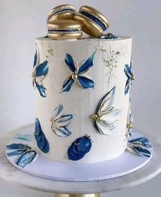 a white and blue wedding cake with gold decorations on the top, sitting on a plate