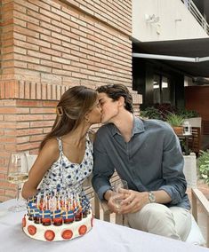 a man and woman kissing in front of a birthday cake with candles on the table