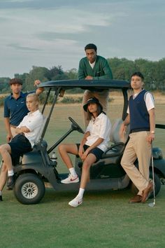 four people sitting in a golf cart with one person standing on the back and two others behind them