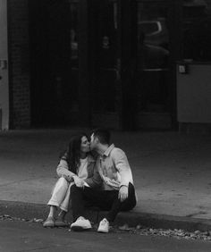 a man and woman sitting on the ground kissing