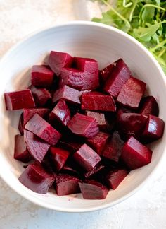 a white bowl filled with chopped beets next to a green leafy plant on a table