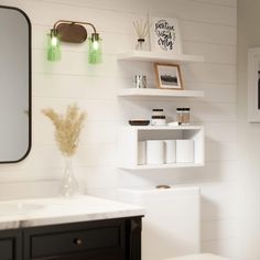 a white toilet sitting next to a sink under a bathroom mirror with shelves above it