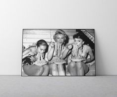 three women eating spaghetti together in front of a wall with a black and white photo on it