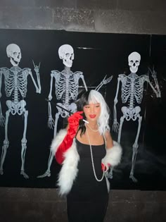 a woman in a black dress and red gloves standing next to a skeleton wall with skeletons on it