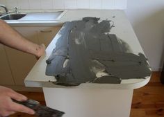 a person painting a kitchen counter top with gray paint