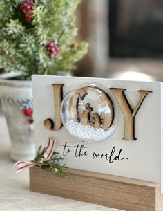 a christmas ornament with the word joy to the world on it and a potted plant in the background