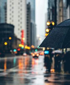 a person holding an umbrella in the rain on a city street with buildings and cars