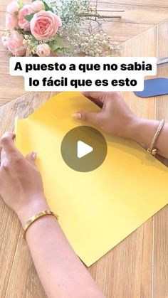 a woman is cutting paper on top of a table with scissors and flowers in the background