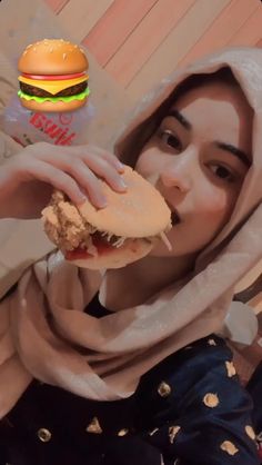 a woman eating a sandwich with a hamburger in front of her face and wearing a headscarf