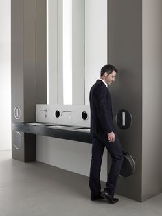 a man standing in front of a mirror next to a wall mounted washbasin