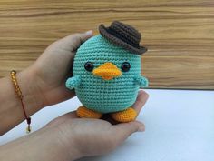 a small crocheted bird with a hat on it's head is being held by a person