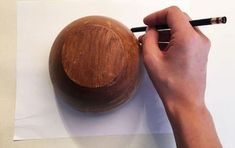 a person writing on paper with a wooden object in front of them and a pencil next to it